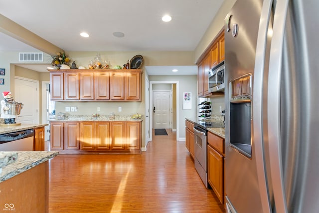 kitchen with appliances with stainless steel finishes, light stone counters, and light hardwood / wood-style flooring