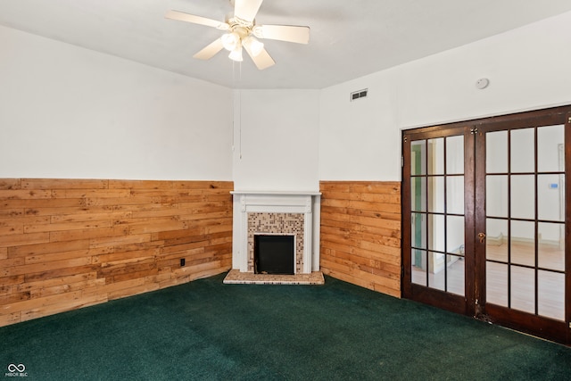 unfurnished living room with wooden walls, a tile fireplace, ceiling fan, and carpet