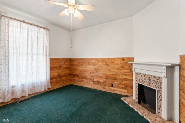 unfurnished living room with wooden walls, a fireplace, ceiling fan, and plenty of natural light