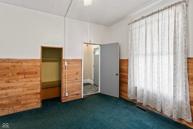 unfurnished bedroom featuring wooden walls, a closet, ceiling fan, and dark carpet