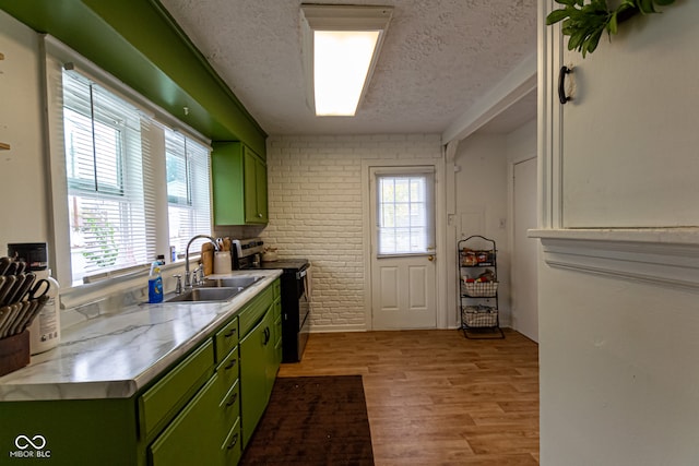 kitchen with sink, green cabinetry, electric range, light hardwood / wood-style floors, and brick wall