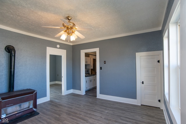 living room featuring dark wood-type flooring, a wood stove, ornamental molding, a textured ceiling, and ceiling fan