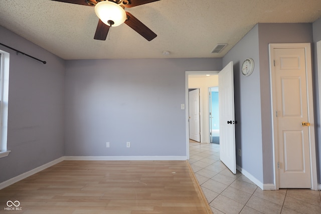 empty room with ceiling fan, a textured ceiling, and light tile patterned floors