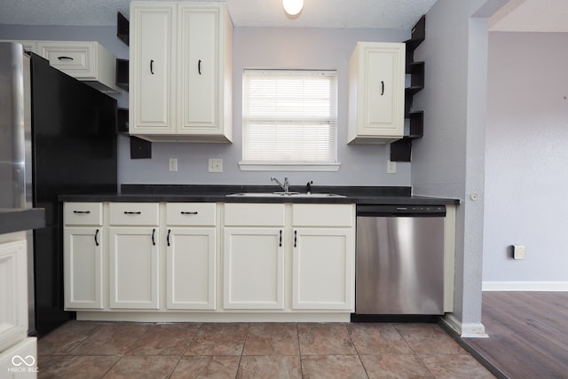 kitchen with dishwasher, black refrigerator, sink, light tile patterned floors, and white cabinetry