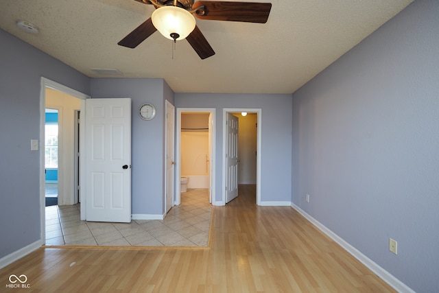 unfurnished bedroom with connected bathroom, a closet, light wood-type flooring, a textured ceiling, and ceiling fan