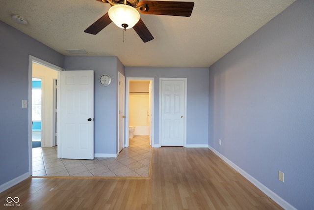 unfurnished bedroom with light wood-type flooring, a textured ceiling, a closet, ceiling fan, and connected bathroom