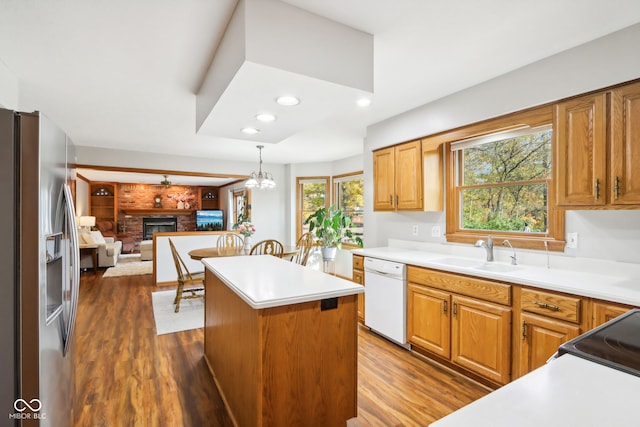 kitchen featuring sink, dishwasher, a kitchen island, a brick fireplace, and stainless steel refrigerator with ice dispenser