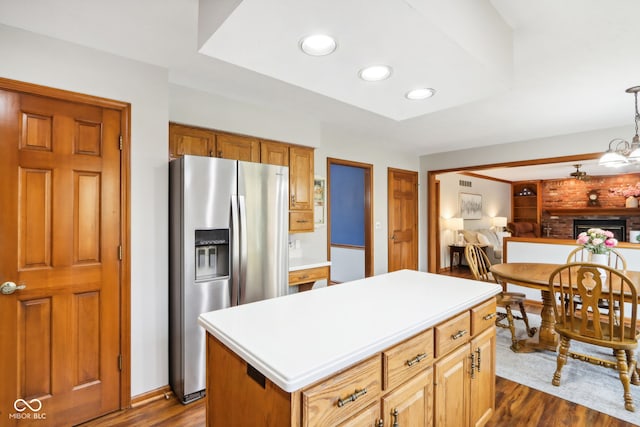 kitchen featuring a kitchen island, dark hardwood / wood-style floors, stainless steel refrigerator with ice dispenser, a brick fireplace, and decorative light fixtures