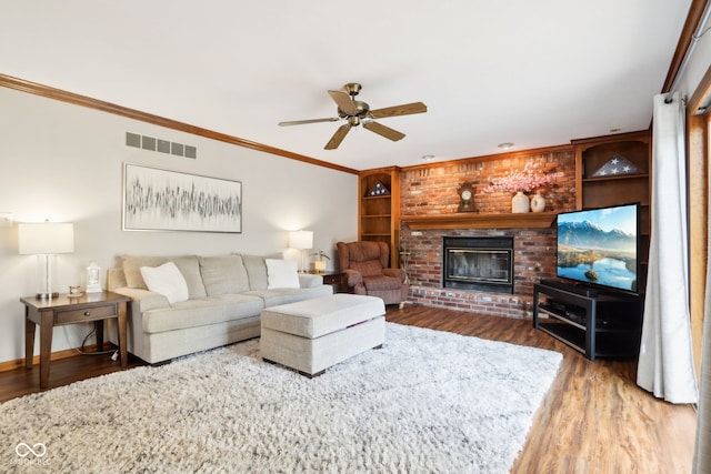 living room with dark wood-type flooring, ceiling fan, ornamental molding, and a fireplace