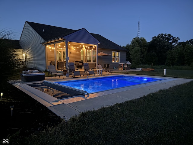 pool at dusk featuring a patio area and a lawn