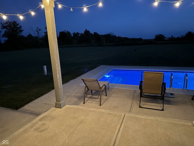 pool at night featuring a patio area and a water view