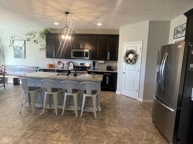 kitchen featuring a center island with sink, appliances with stainless steel finishes, a chandelier, pendant lighting, and light stone counters