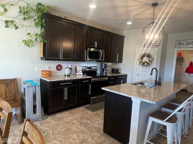 kitchen featuring appliances with stainless steel finishes, sink, hanging light fixtures, light stone counters, and a kitchen island with sink