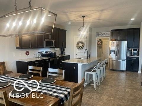kitchen with a breakfast bar, a sink, an island with sink, stainless steel appliances, and pendant lighting