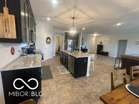 kitchen with open floor plan, a kitchen bar, dark cabinets, a sink, and stainless steel appliances