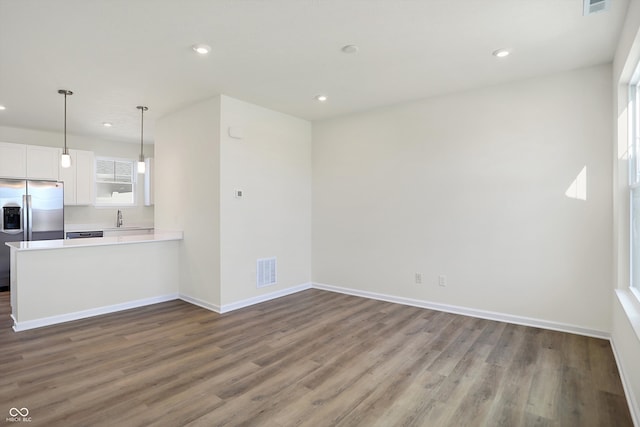 kitchen featuring dark hardwood / wood-style flooring, kitchen peninsula, stainless steel fridge, white cabinetry, and decorative light fixtures