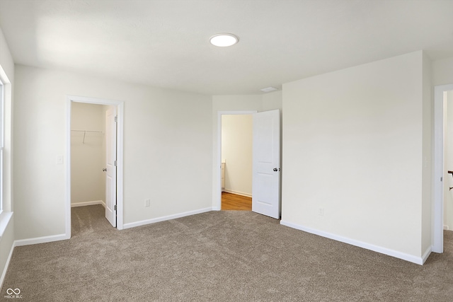 unfurnished bedroom with a walk in closet, a closet, and carpet flooring