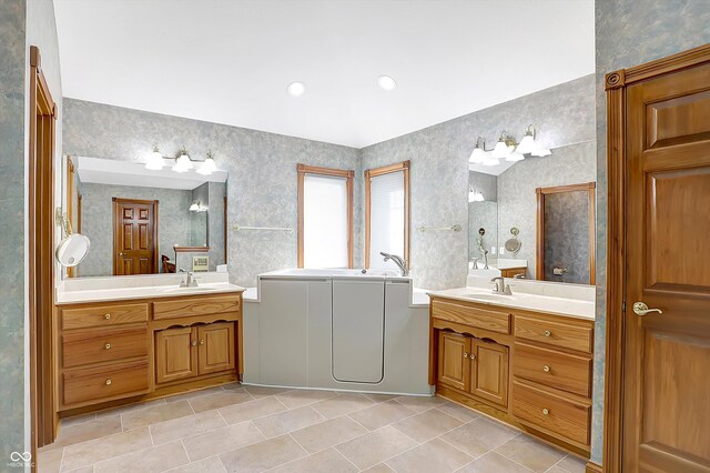 full bath featuring two vanities, a sink, and wallpapered walls