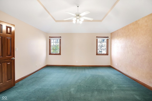 carpeted empty room with ceiling fan, baseboards, and a raised ceiling