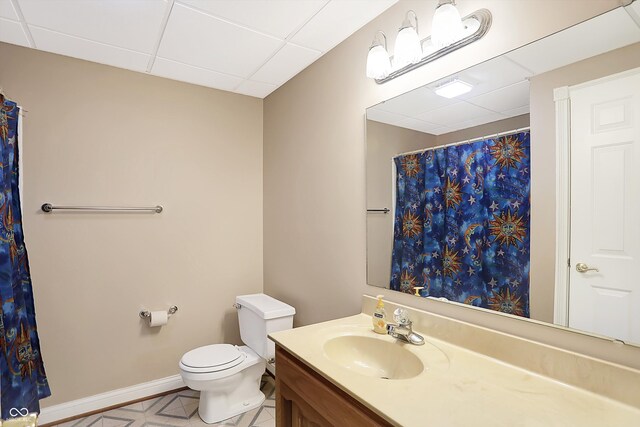 full bathroom featuring toilet, baseboards, a drop ceiling, and vanity