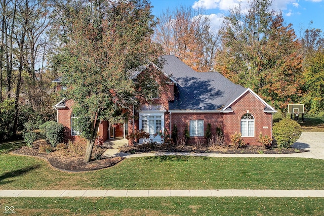 view of front facade featuring a shingled roof, a front lawn, and brick siding