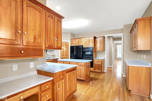 kitchen featuring brown cabinetry, a center island, light countertops, and black appliances