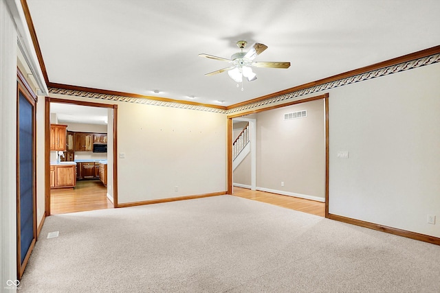 empty room featuring light colored carpet, visible vents, ornamental molding, a ceiling fan, and baseboards