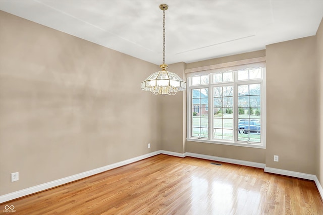 unfurnished room with visible vents, light wood finished floors, baseboards, and an inviting chandelier