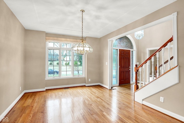 entrance foyer featuring a notable chandelier, stairway, baseboards, and light wood-style floors