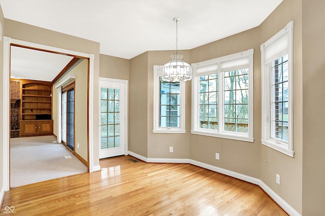 unfurnished dining area with light wood-style floors, visible vents, a notable chandelier, and baseboards