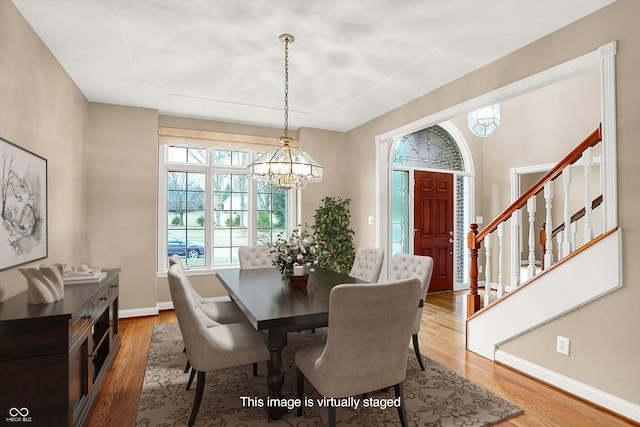 dining room featuring stairs, baseboards, a chandelier, and wood finished floors