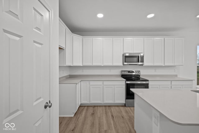 kitchen with white cabinets, appliances with stainless steel finishes, and light wood-type flooring