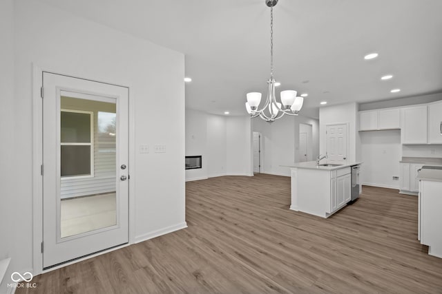 kitchen featuring dishwasher, pendant lighting, light hardwood / wood-style floors, a center island with sink, and white cabinets