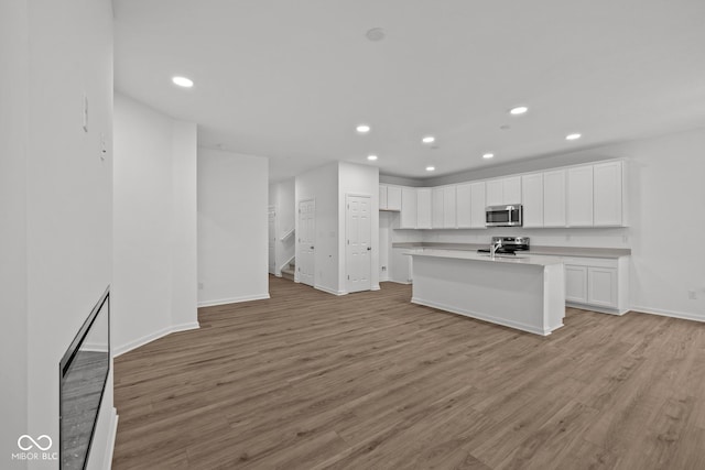 kitchen with a center island with sink, white cabinets, light hardwood / wood-style flooring, and appliances with stainless steel finishes