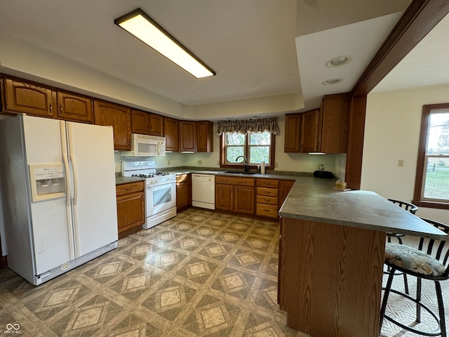 kitchen featuring a wealth of natural light, sink, a kitchen breakfast bar, and white appliances