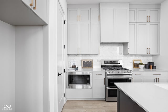 kitchen with white cabinetry, light wood-type flooring, backsplash, and appliances with stainless steel finishes