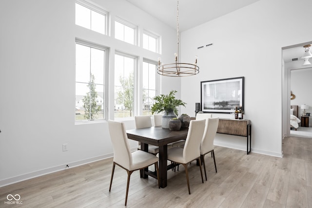 dining area featuring a notable chandelier, light hardwood / wood-style floors, and a high ceiling