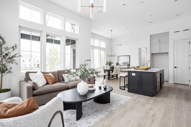 living room featuring ceiling fan with notable chandelier, light hardwood / wood-style floors, a towering ceiling, and sink