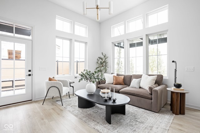 living room featuring light wood-type flooring, a high ceiling, and an inviting chandelier