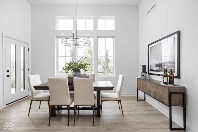 dining area featuring a wealth of natural light, light hardwood / wood-style flooring, a towering ceiling, and an inviting chandelier