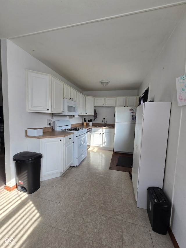 kitchen with white cabinetry, sink, light tile patterned floors, and white appliances