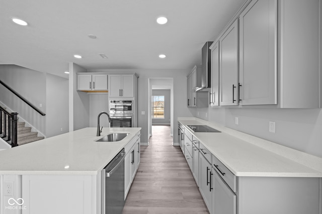 kitchen featuring a center island with sink, appliances with stainless steel finishes, sink, light hardwood / wood-style floors, and wall chimney exhaust hood