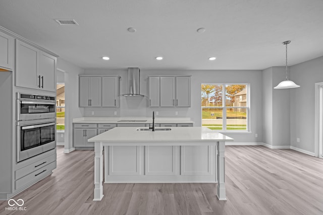 kitchen with gray cabinets, wall chimney range hood, sink, and light hardwood / wood-style flooring