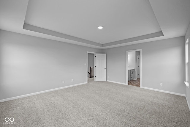 unfurnished bedroom with ensuite bath, carpet floors, and a tray ceiling