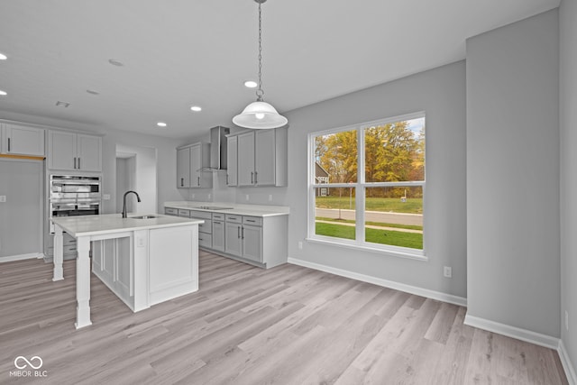 kitchen with gray cabinets, pendant lighting, sink, wall chimney exhaust hood, and a kitchen island with sink