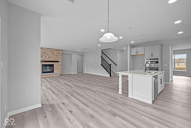 kitchen with decorative light fixtures, an island with sink, light hardwood / wood-style floors, and a fireplace