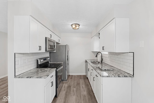 kitchen with white cabinetry, sink, light stone counters, and appliances with stainless steel finishes