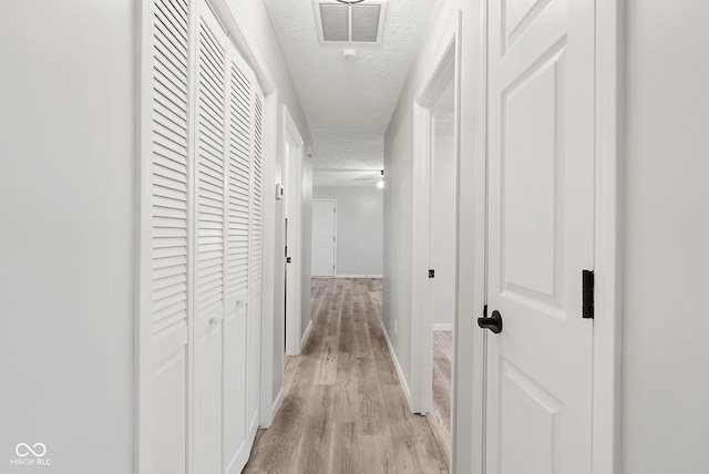 hall with light wood-type flooring and a textured ceiling