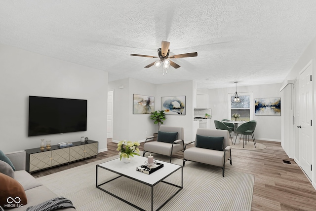 living room with ceiling fan with notable chandelier, a textured ceiling, and light wood-type flooring