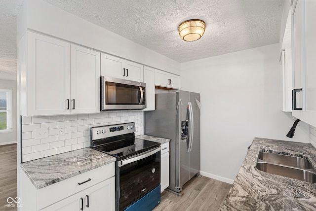 kitchen with white cabinets, stainless steel appliances, light hardwood / wood-style flooring, and light stone countertops